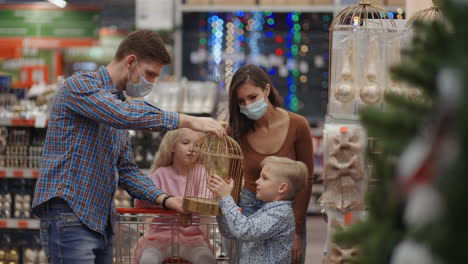A-happy-family-in-medical-masks-in-the-store-buys-Christmas-decorations-and-gifts-in-slow-motion.-Four-people-father-son-daughter-and-mother